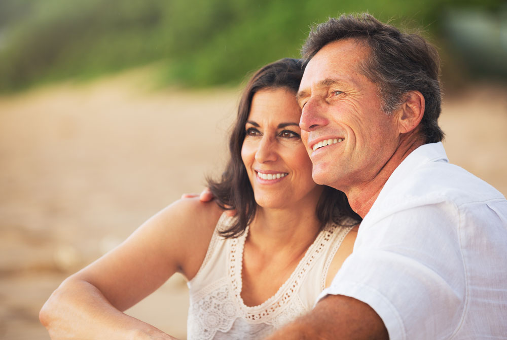 removing Senior couple sitting on the beach with their arms around each other